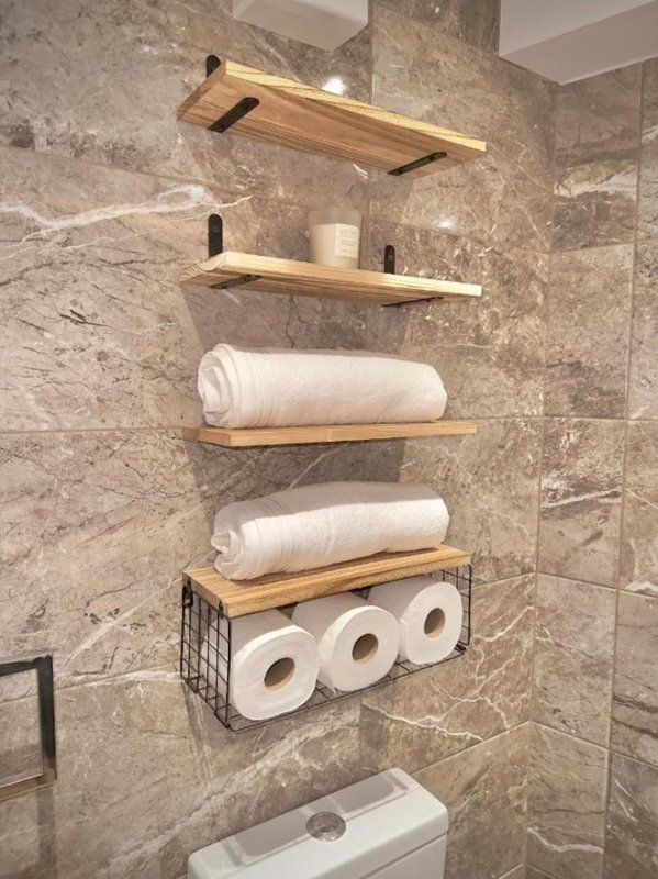 Bathroom wall with wooden shelves, toilet paper rolls, and wire storage basket