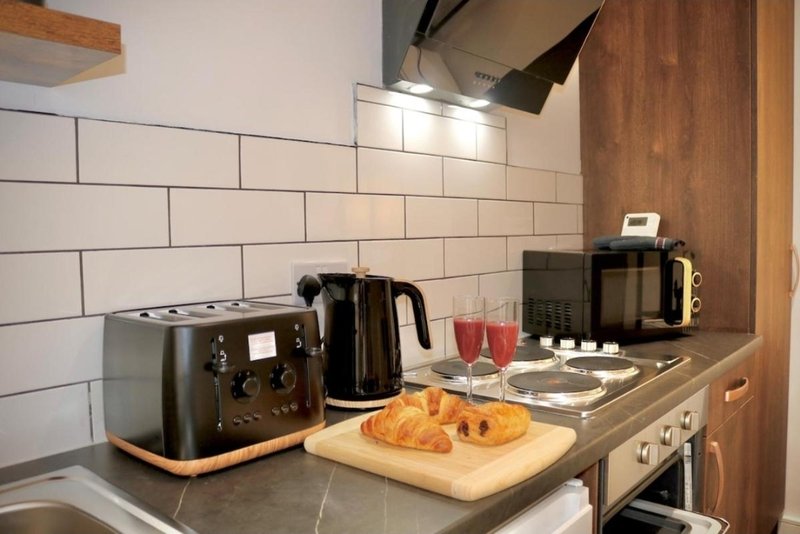 Kitchen countertop with toaster, kettle, croissants, and cooking appliances under subway tile backsplash