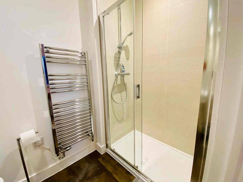 Modern bathroom with walk-in shower, glass enclosure, heated towel rail, and dark flooring