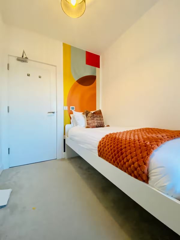 Modern bedroom with single bed, orange bedding, abstract wall art, and white door