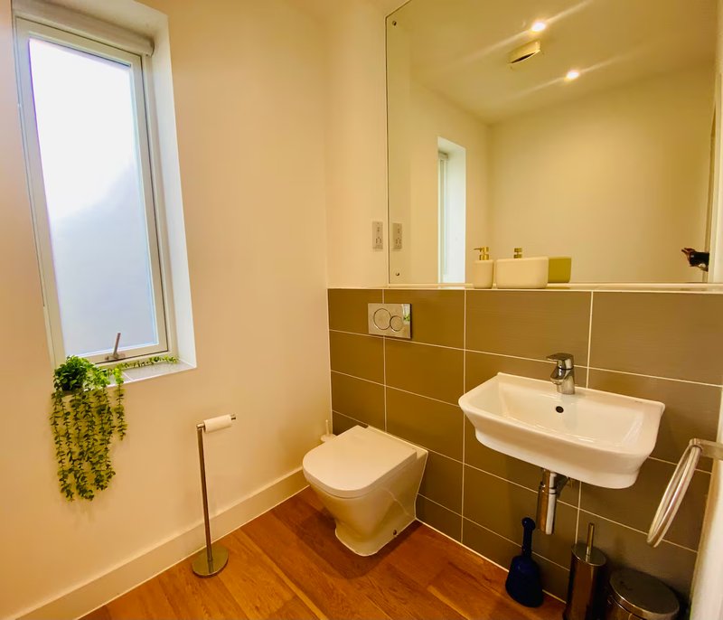 Modern bathroom with olive-green tiled walls, white sink, toilet, mirror and window