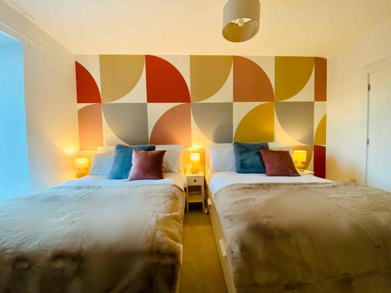 Modern bedroom with two beds, colorful geometric headboard, bedside lamps and pendant light