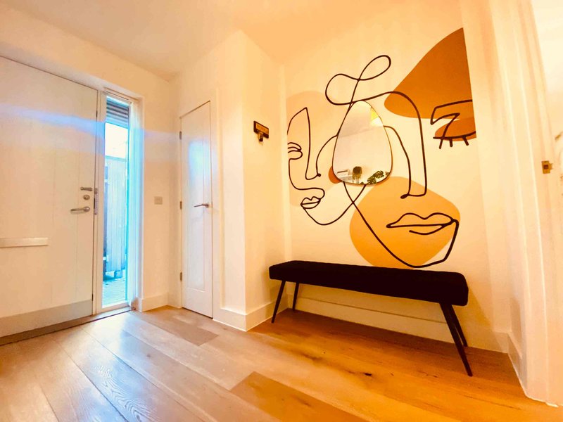 Bright hallway with wooden floor, modern wall art, black bench and glass door entry
