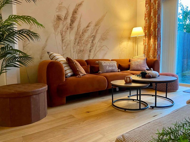 Modern living room with terracotta curved sofa, wooden tables, plants and warm lighting