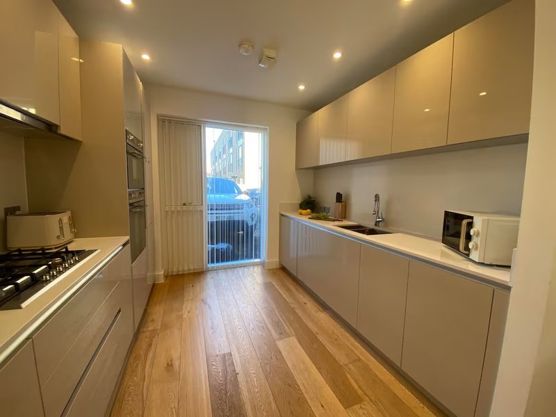 Modern kitchen with cream cabinetry, wooden flooring, and glass balcony doors