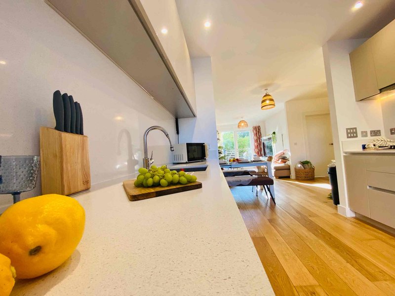 Modern kitchen with white countertop, wooden knife block, fresh fruit, and view into living area
