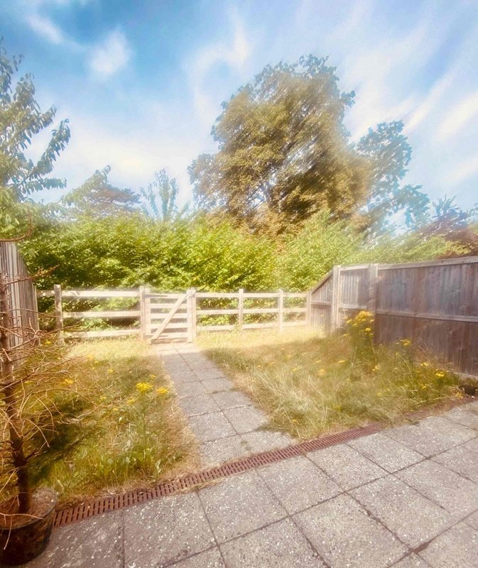 Exterior garden area with wooden gate, paved pathway, and mature trees