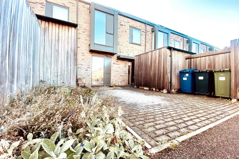 Modern brick and metal-clad townhouse exterior with paved courtyard, wooden fence and bins