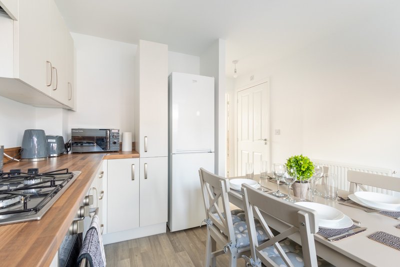 Modern kitchen with white cabinets, wooden countertop, gas hob, and dining table with chairs
