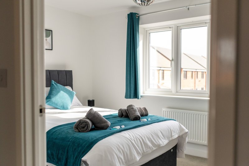 Modern bedroom with double bed, teal bedding, rolled towels, and bay window with curtains