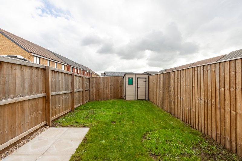 Enclosed garden with wooden fencing, green lawn, paved patio and storage shed