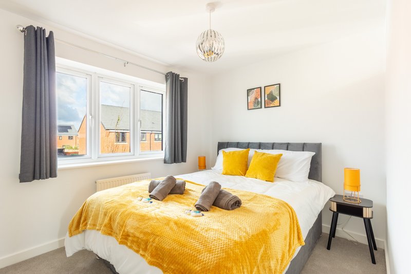 Bright bedroom with double bed, yellow bedding, grey headboard and modern pendant light