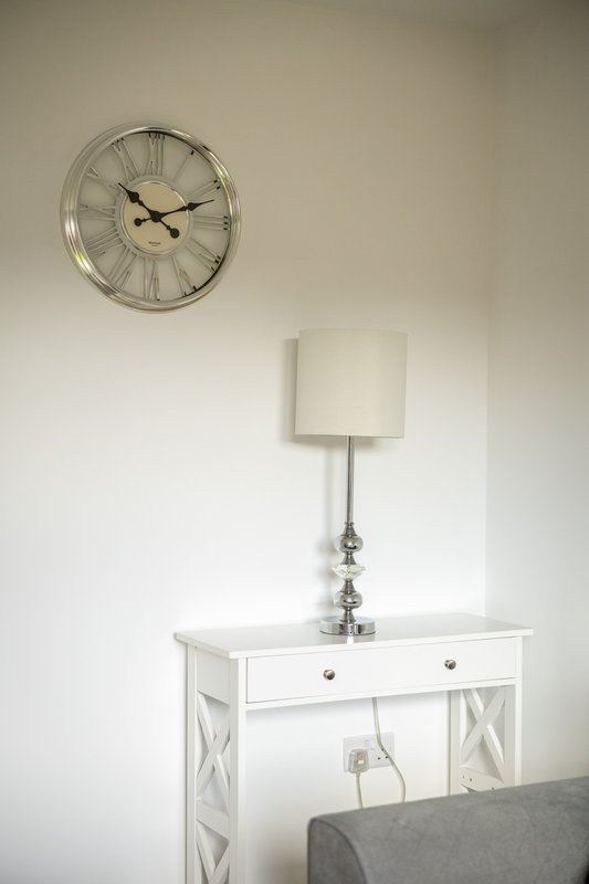 Bedroom corner with white desk, table lamp, wall clock, and gray upholstered furniture