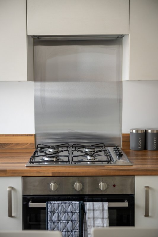 Modern kitchen with gas hob, stainless steel splashback and white cabinetry