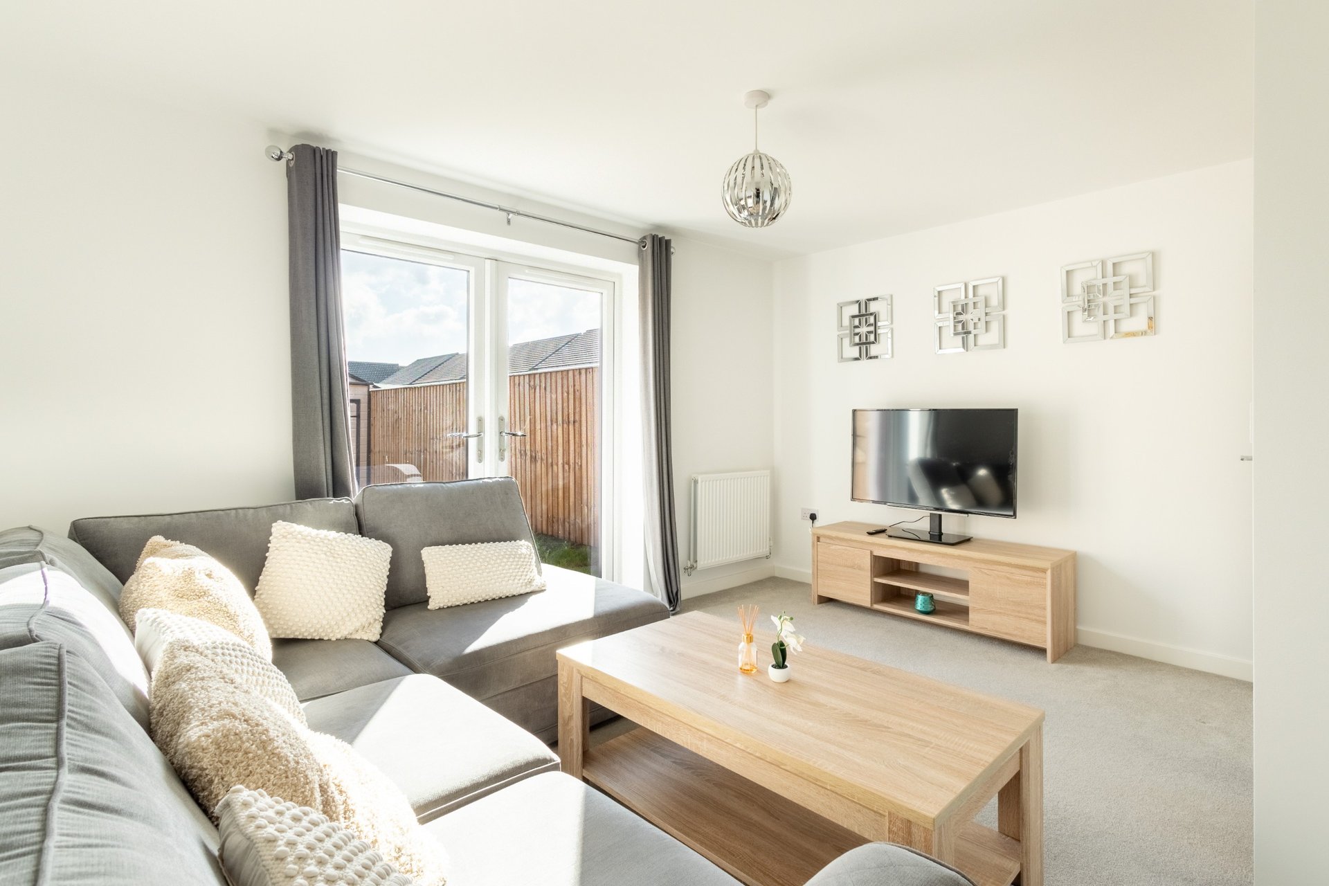 Bright living room with gray sofa, wooden coffee table, TV stand and patio doors