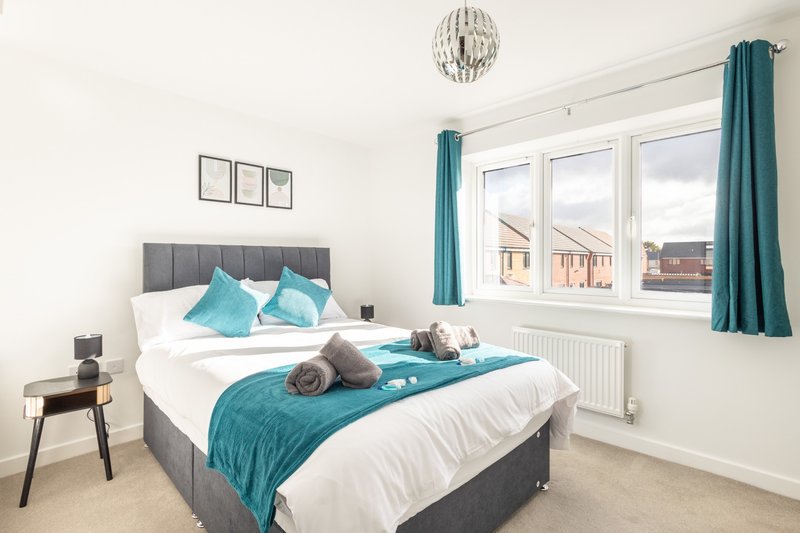 Bright bedroom with double bed, turquoise bedding, grey headboard and large window with street view