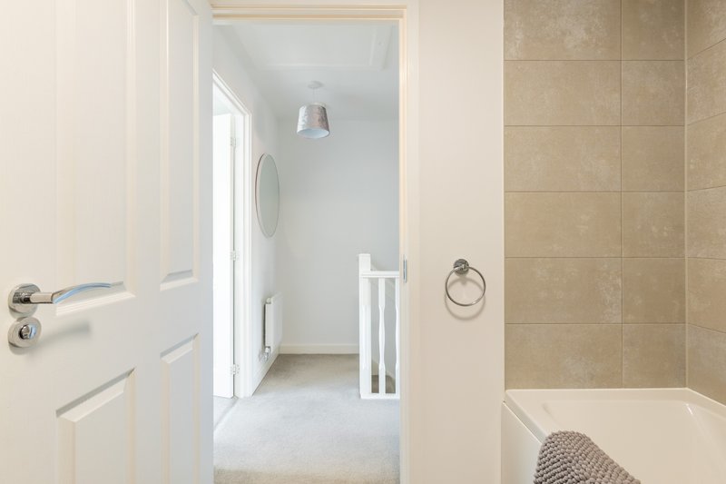 Modern bathroom with beige tile walls, white bathtub, and door to hallway