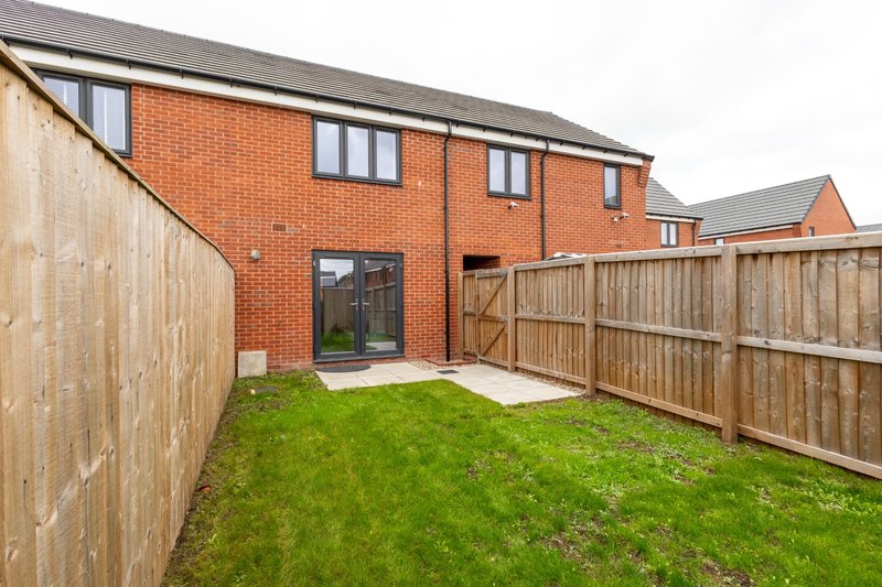 Modern brick house with patio door, green lawn, and wooden fencing on both sides