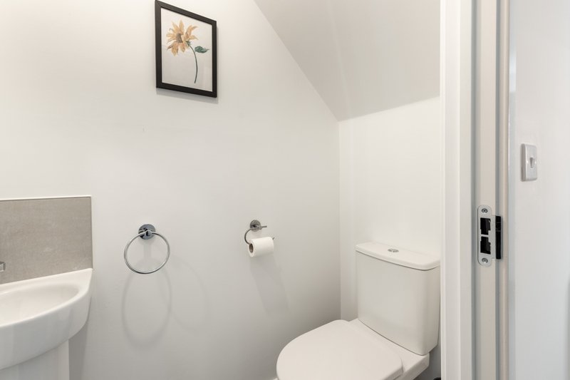 Clean modern bathroom with white toilet, sink, towel ring and framed wall art