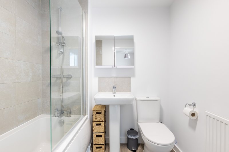 Clean modern bathroom with shower, toilet, sink, mirror cabinet and woven storage baskets