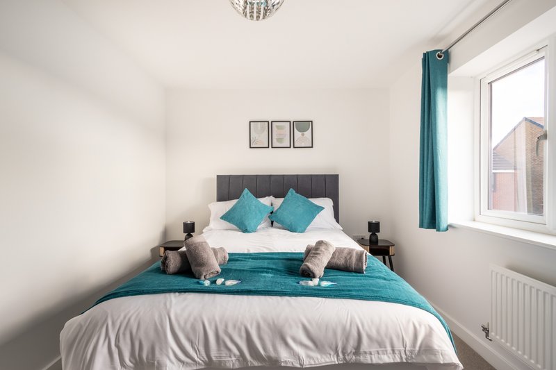 Modern bedroom with double bed, teal bedding, white pillows and decorative cushions