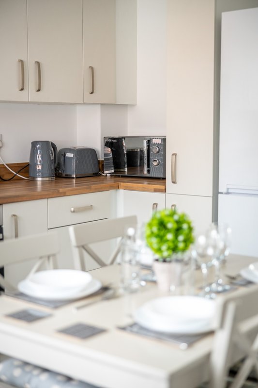 Modern kitchen with white cabinetry, wooden worktop, and dining table set for two