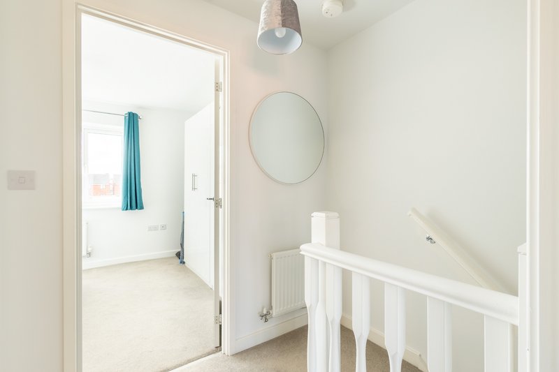 Bright hallway with white walls, round mirror, pendant light and staircase railing