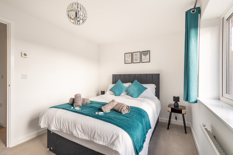 Modern bedroom with double bed, teal bedding, white pillows, pendant light and side table