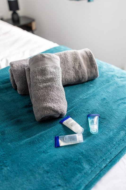 Bed with teal blanket, rolled towels and toiletry samples
