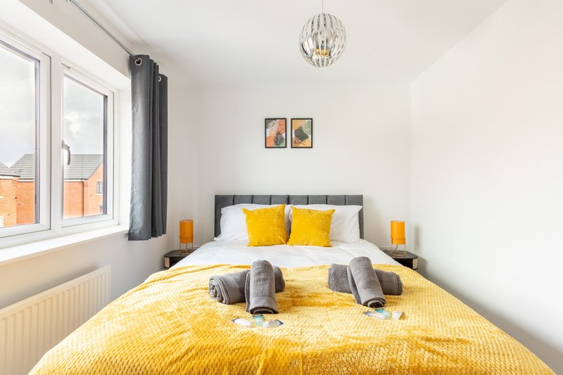 Bright bedroom with double bed, yellow bedding, grey headboard and pendant light fixture