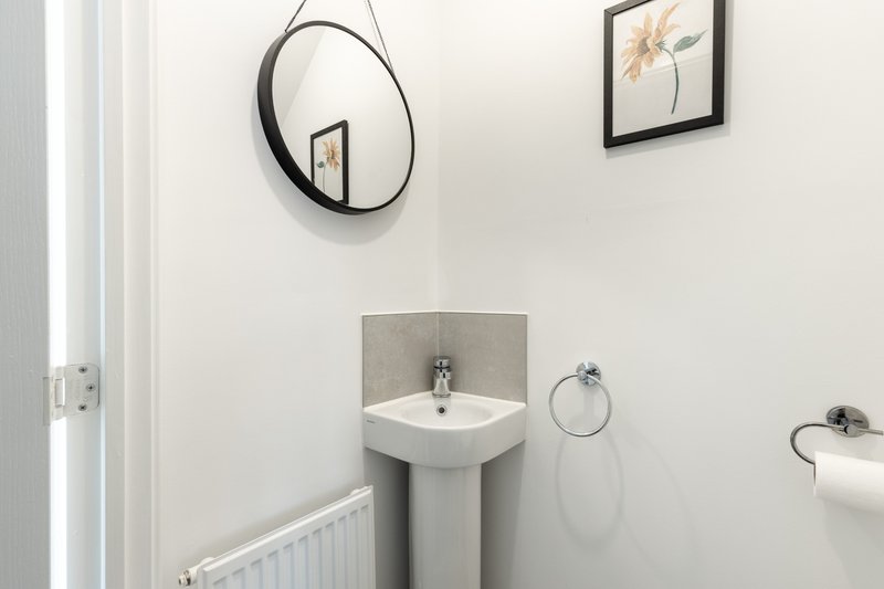 Modern bathroom with pedestal sink, round mirror, radiator and wall art