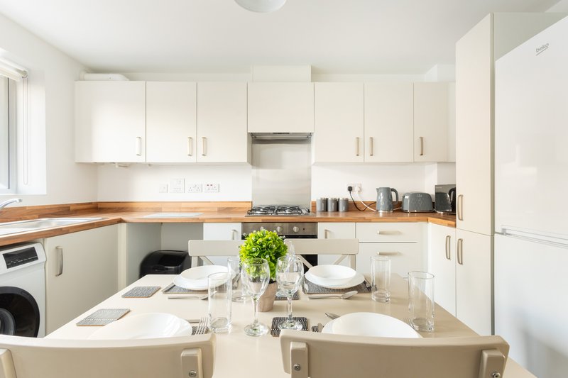 Modern white kitchen with dining table, wooden worktop, integrated appliances and green plant centerpiece