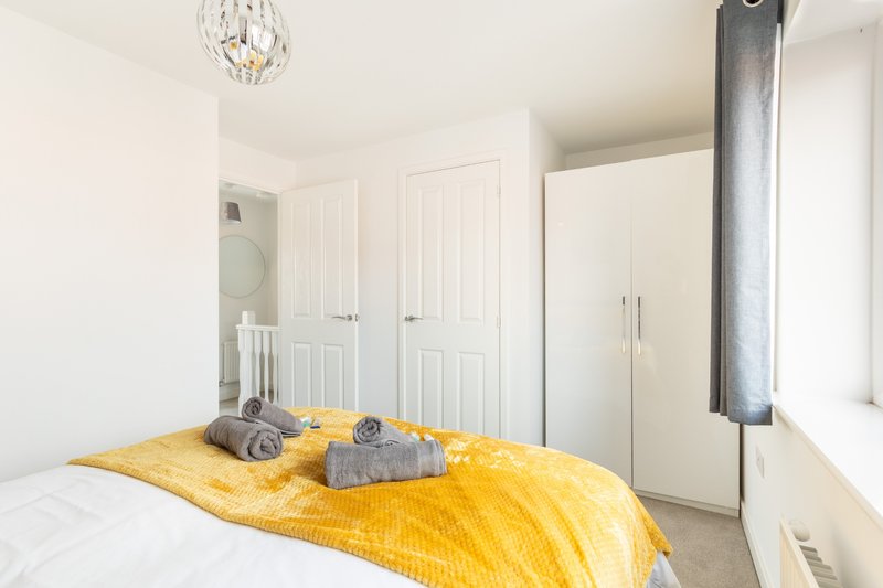 Bright bedroom with double bed, yellow throw, grey cushions and built-in wardrobes