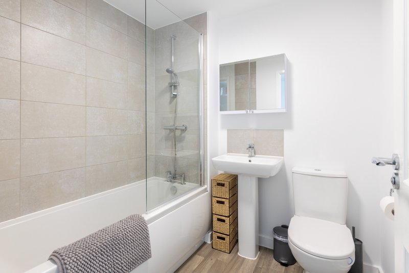 Modern bathroom with shower enclosure, pedestal sink, toilet and woven storage baskets