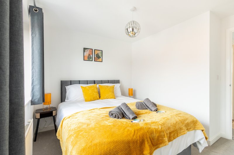 Bright bedroom with double bed, yellow bedding, grey headboard, pendant light, and wall art