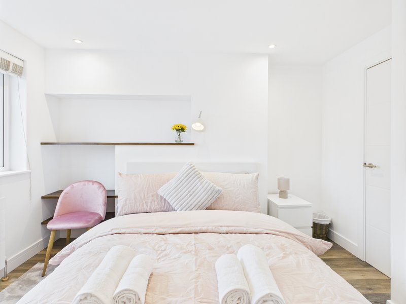 Bright bedroom with double bed, pink cushion, wooden flooring and white walls