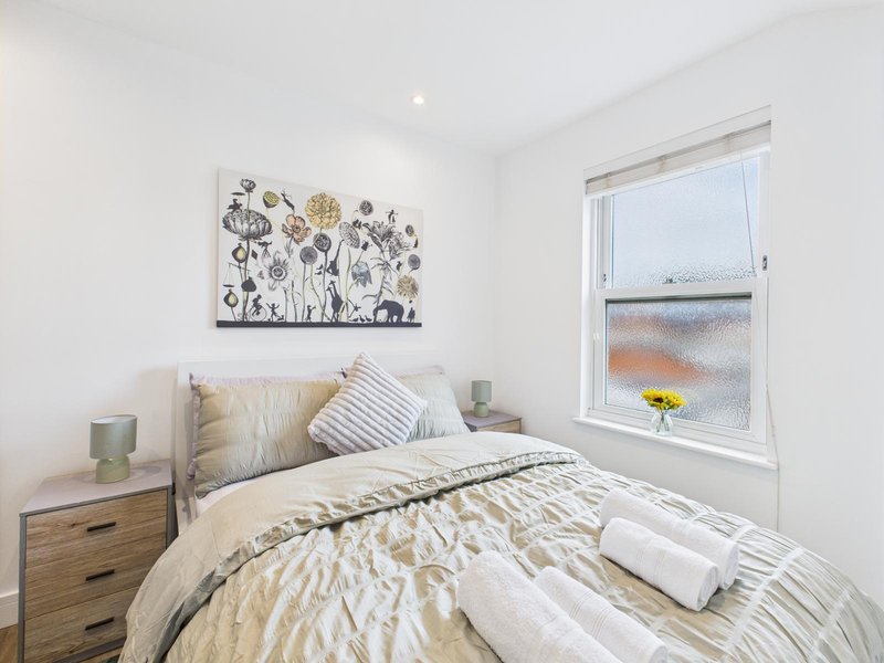 Bright bedroom with double bed, wooden nightstand, wall art, and large window with garden view