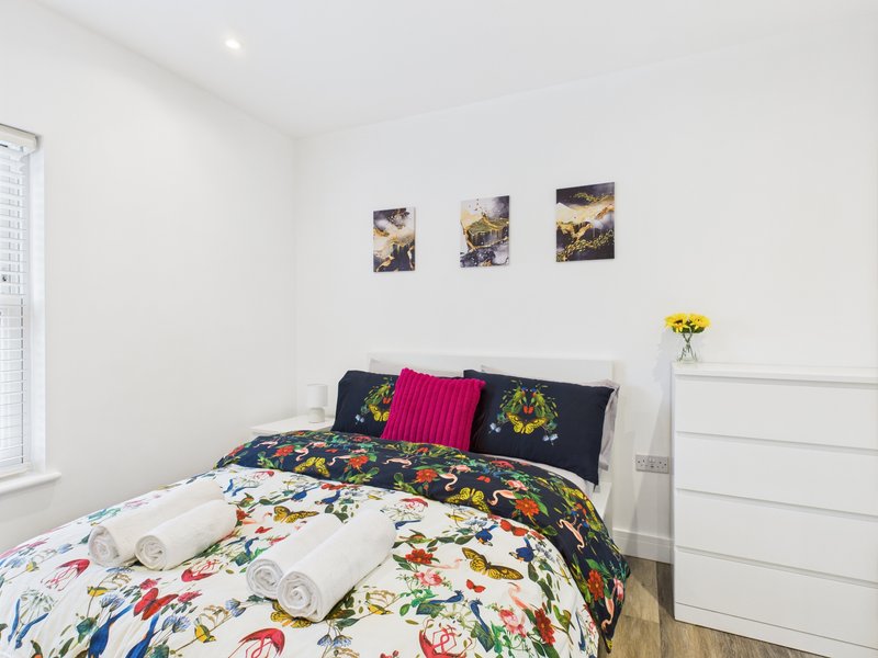Modern bedroom with double bed, colorful floral bedding, pink cushion, and framed wall art