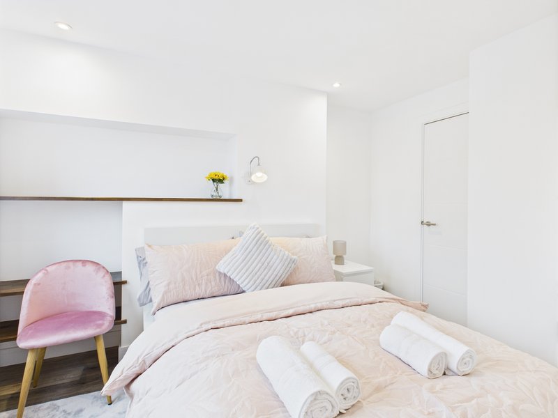 Modern bedroom with double bed, pink chair, shelf with flowers and white walls