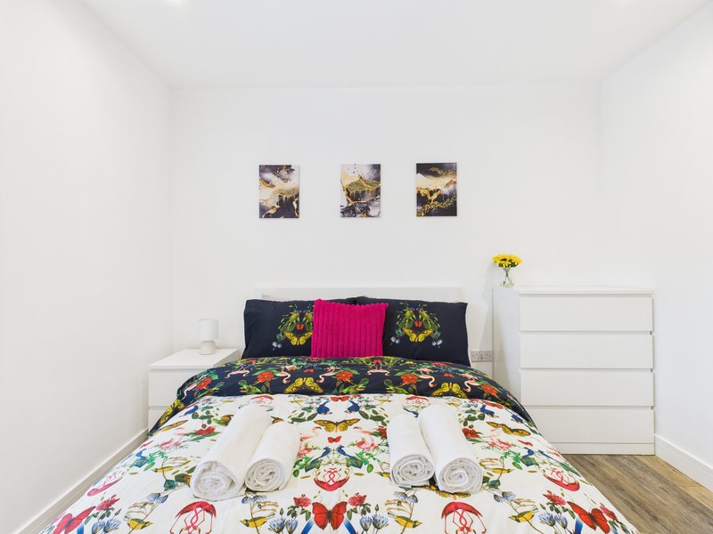 Bedroom with colorful butterfly-patterned bedding, pink pillow, white dresser, and framed wall art