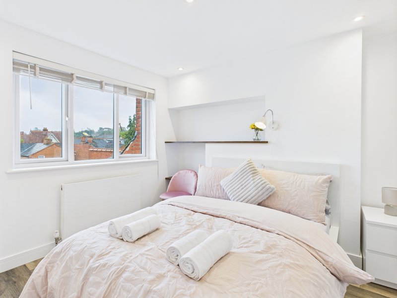 Bright bedroom with double bed, pink pillows, large window overlooking rooftops