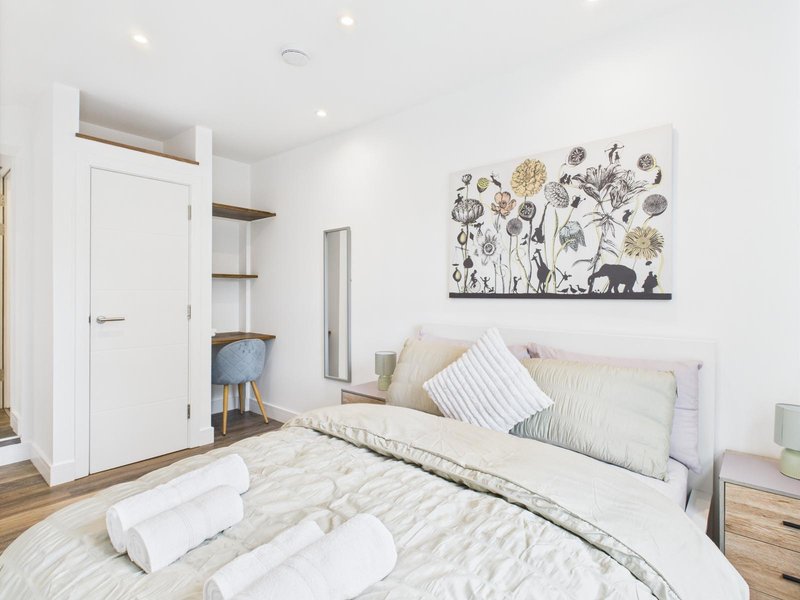 Bright bedroom with double bed, white bedding, wooden nightstand and wall art
