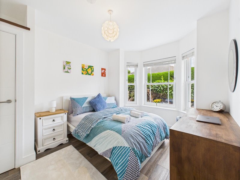 Bright bedroom with double bed, blue striped bedding, white nightstand, wooden desk and garden views