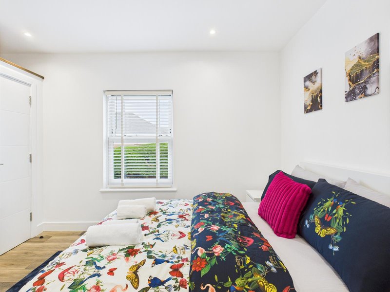 Bright bedroom with double bed, colorful patterned bedding, pink and navy cushions, wooden floor and window with shutters