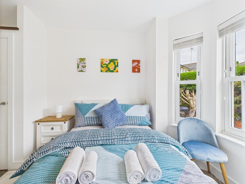 Bright bedroom with double bed, blue bedding, rolled towels, blue chair and garden view