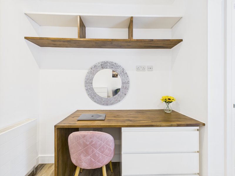 Modern bedroom workspace with wooden desk, pink chair, round mirror and wooden shelving