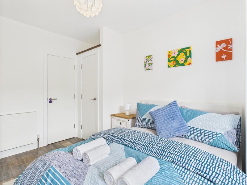 Bright bedroom with blue striped bedding, white pillows, wooden nightstand and colorful wall art
