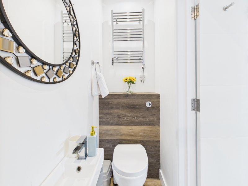 Compact bathroom with white toilet, wooden vanity, decorative mirror and towel rail