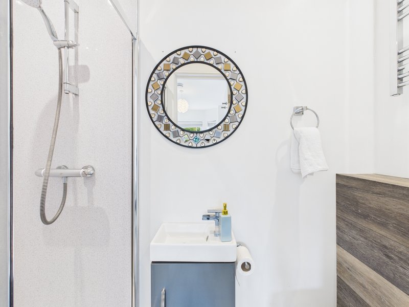 Modern bathroom with walk-in shower, blue vanity sink, decorative round mirror and towel rail