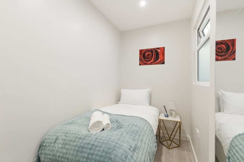 Compact bedroom with single bed, rolled towel, bedside table and red rose wall art